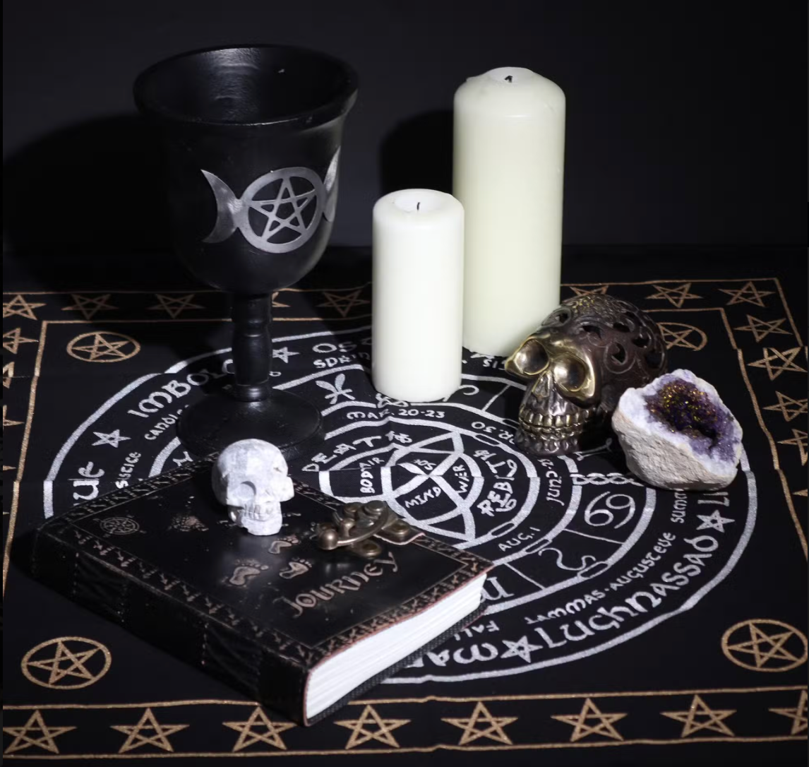 Witchcraft altar setup with black goblet, candles, skull, and amethyst on a black and gold rune cloth.