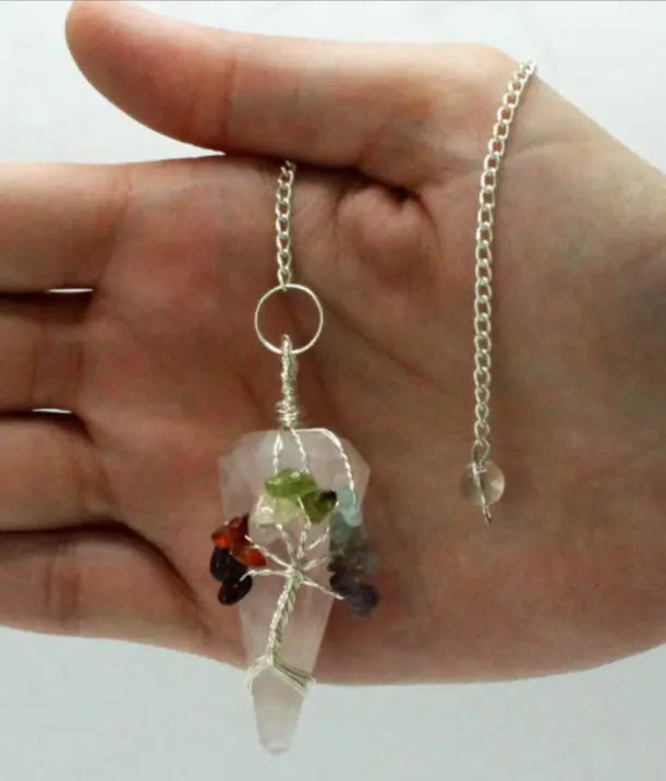 Hand holding a crystal pendant necklace with colored stones on a plain background