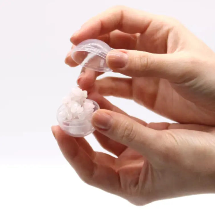 Hand holding a small transparent container with a white object inside on a white background