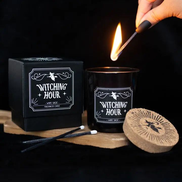 Witching Hour candle being lit with packaging and matches on a dark background