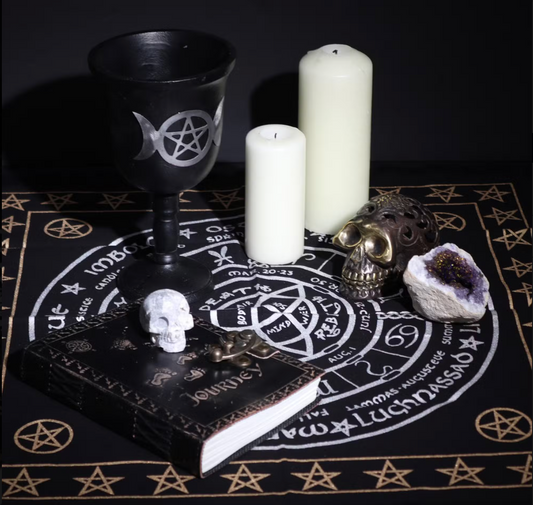 Witchcraft altar setup with black goblet, candles, skull, and amethyst on a black and gold rune cloth.