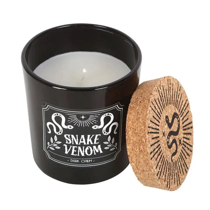 Candle in a black container with 'Snake Venom' label and cork lid on a white background
