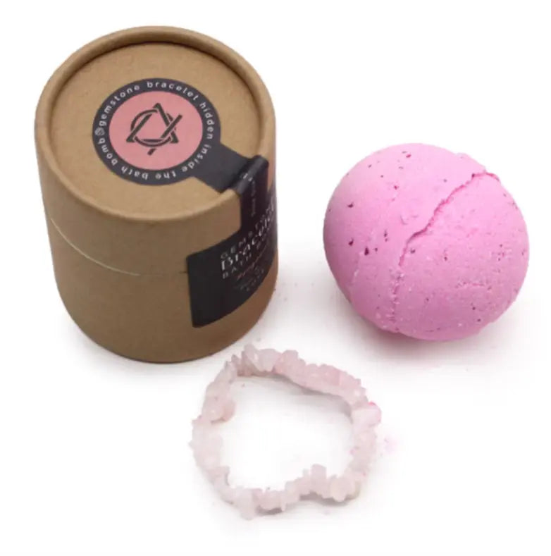 Pink bath bomb with a brown cardboard container and a pink crystal bracelet on a white background