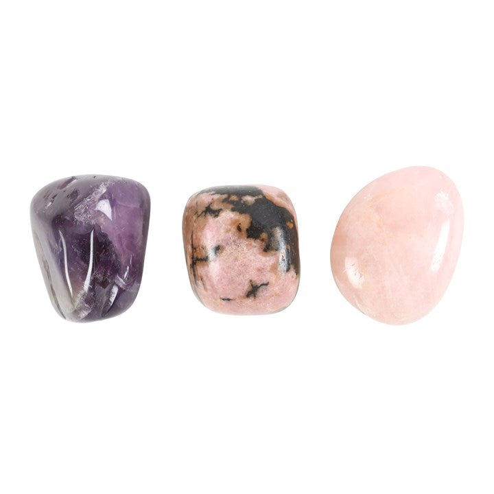 Three tumbled stones, amethyst, rhodonite, and rose quartz, arranged in a line, displaying deep purple and pink colours' with natural veining.